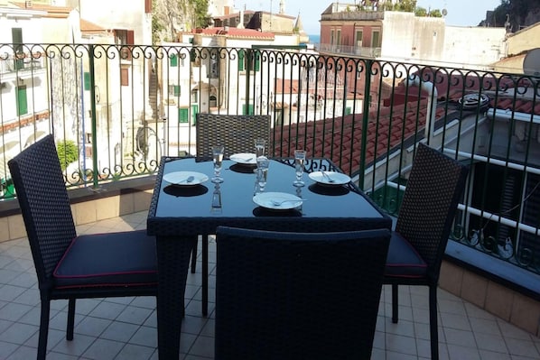 A balcony with a table set for four, surrounded by wicker chairs, overlooking a cityscape.