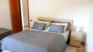 A neatly made bed with a grey quilt, a wooden headboard, and a bedside table with a lamp. - Cetara House 1 on Amalfi Coast (Cetara)