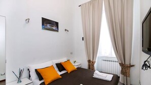 A hotel room with a bed, white nightstand, and a window with curtains. - Roman 2BR Apartment @ 2min near Vatican Museums & 8 min Basilica St.Peter's (Roma)