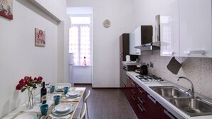 A modern kitchen with white cabinets, stainless steel appliances, and a dining area with a table set for two. - Roman 2BR Apartment @ 2min near Vatican Museums & 8 min Basilica St.Peter's (Roma)