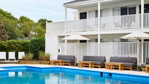 A two-story building with a pool area featuring lounge chairs and umbrellas. -  Parker Beach Lodge (South Yarmouth)