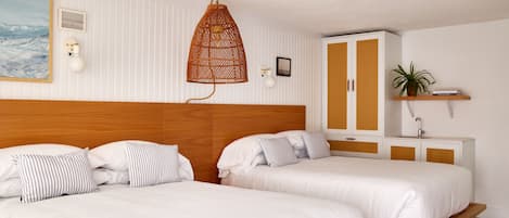 A hotel room with two beds, a wooden headboard, a white-striped pillow, a hanging wicker lamp, a white cabinet with a shelf, and a framed picture on the wall.
