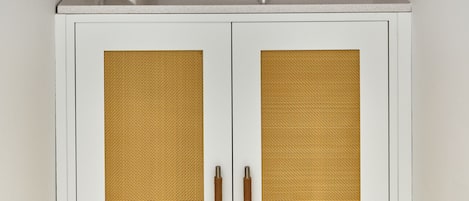 Eine Küche mit Spüle, einem weißen Schrank mit strukturierter Tür, einem Edelstahlkochtopf, einer weißen Vase mit grünen Blättern und einem Holzregal mit Schüsseln und Tellern.