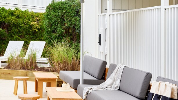 A patio area with a sofa, wooden tables, and chairs, surrounded by white umbrellas. -  Parker Beach Lodge (South Yarmouth)