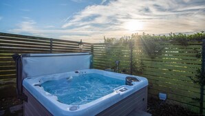 A hot tub in a backyard with a wooden fence and a clear sky.