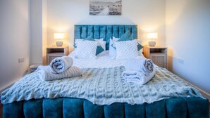 A neatly made bed with a blue headboard, two bedside lamps, and a framed picture above.