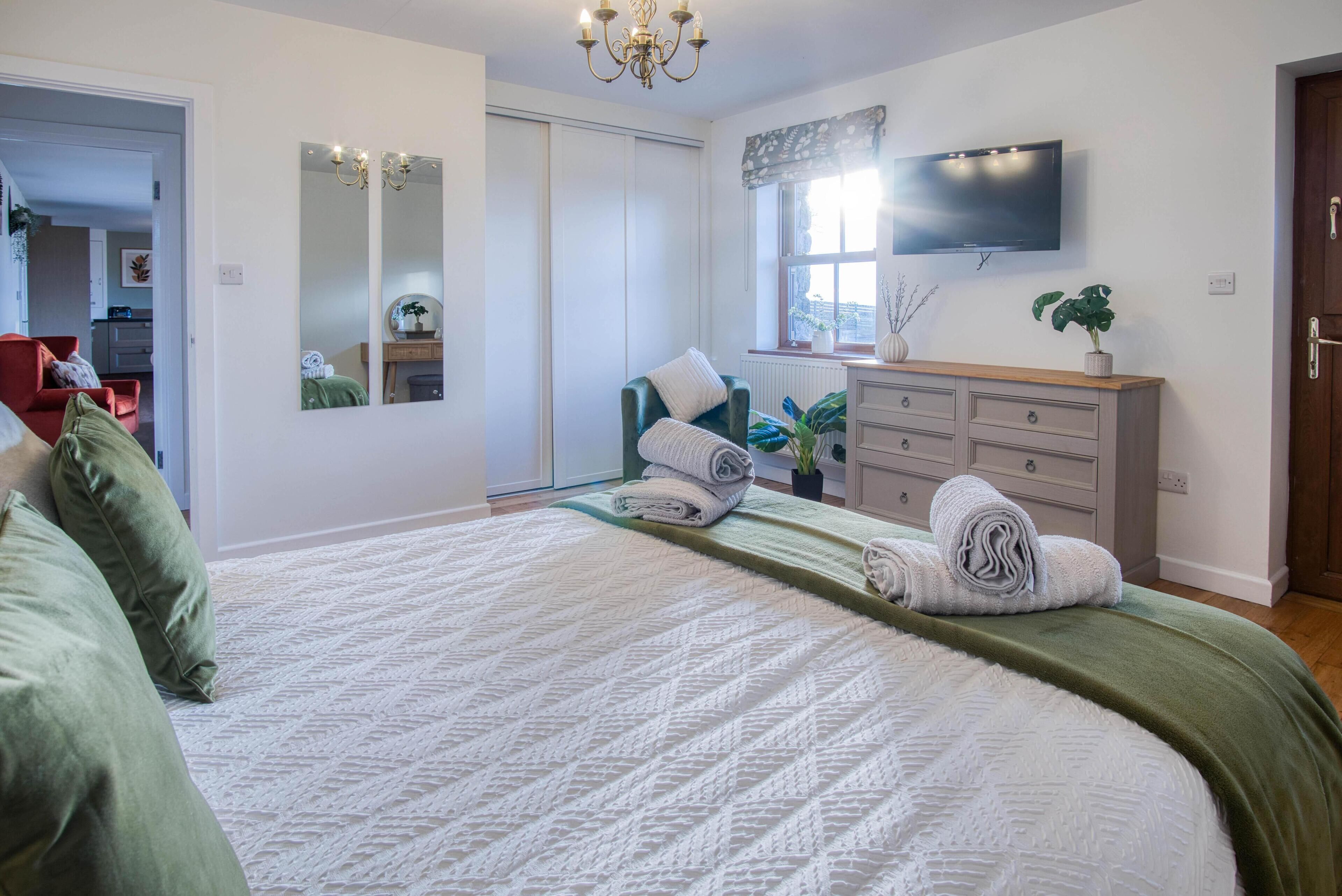 A bedroom with a large bed, a dresser, a TV, and a mirror.