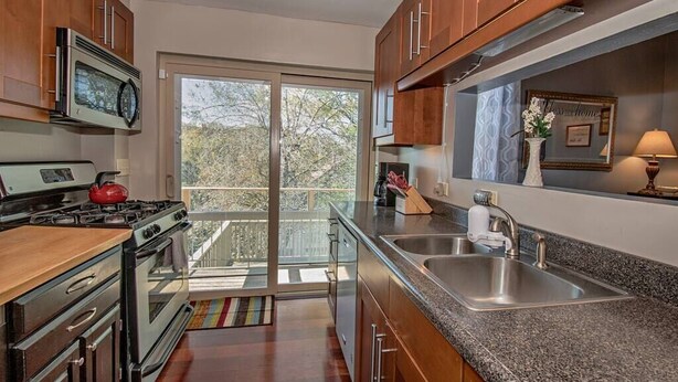 A modern kitchen with wooden cabinets, a stainless steel sink, and a large window overlooking a balcony. - Updated Victorian - Serene Backyard + City Access (Pittsburgh)