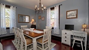 A dining room with a wooden table, white chairs, a chandelier, and a television on a white dresser. - Updated Victorian - Serene Backyard + City Access (Pittsburgh)
