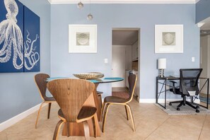 A dining area with a round table, chairs, and artwork on the wall.