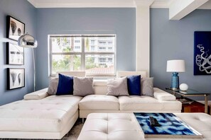 A modern living room with a sectional sofa, a coffee table with a remote control, a side table with a lamp, and artwork on the walls.