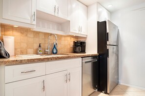 A modern kitchen with white cabinets, a stainless steel refrigerator, a coffee maker, and a sink with a faucet.