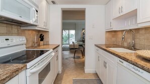 Una cocina moderna con armarios blancos, microondas integrado, estufa y pileta.