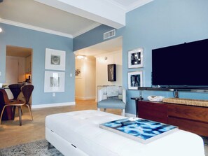 Un salon moderne doté d’un grand téléviseur à écran plat, d’un canapé blanc et d’une table basse au motif abstrait bleu.