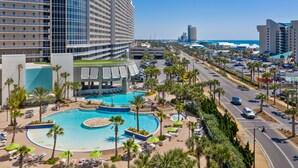 A hotel with a large pool, palm trees, and a view of the city.