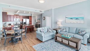 A modern living room with a light blue sofa, a wooden coffee table, and a dining area with a wooden table and chairs.