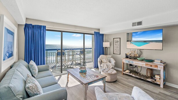 A spacious living room with a balcony overlooking the sea, a comfortable sofa, a coffee table, and a wooden console table with decorative items. - The Oceans 405- 2 Bed OF Condo with Pool (North Myrtle Beach)