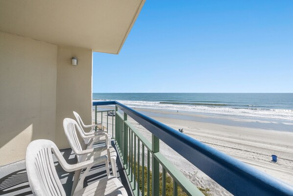 A balcony with white plastic chairs and a view of the beach.