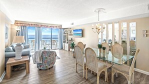 A spacious living room with a dining area, large windows, and a view of the ocean.