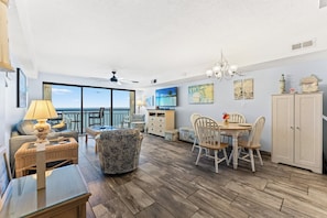 A spacious living area with a balcony, a dining table with chairs, a TV, and a cabinet.