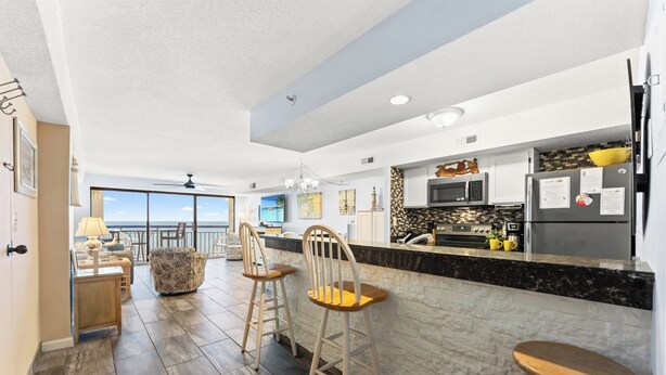 A modern kitchen with a bar area, a dining area with a view, and a ceiling fan.