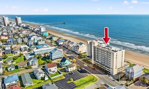 Ein Küstenwohngebiet mit einem markanten Hotel, das einen Dachpool, eine in den Ozean führende Mole und einen klaren Blick auf den Strand bietet.