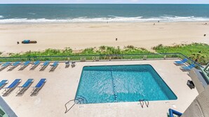 A swimming pool with lounge chairs, a view of the beach, and a lifeguard tower.