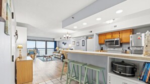 Une cuisine moderne avec des meubles en bois, un four à micro-ondes, un réfrigérateur et une plaque de cuisson. On y trouve des tabourets de bar verts et un coin repas avec vue.