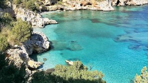 Een kustlandschap met helder turquoise water, rotsachtige kliffen en schaarse begroeiing.