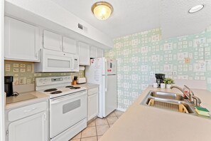 A kitchen with white appliances, a tiled backsplash, and a sink with a faucet. - Oceans 814 - Ocean Front 1 Bedroom Condo in Cherry Grove (North Myrtle Beach)