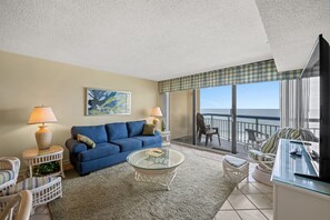 Relax in this inviting living room with a sofa, coffee table, and wicker chairs, offering a view of the ocean.