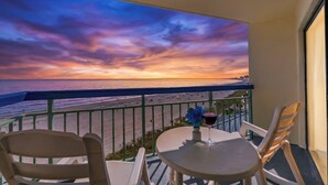A balcony with a table and chairs, overlooking a beach with a sunset view. - Oceans 816 - Great Views - 1 Bedroom Ocean Front Condo (North Myrtle Beach)
