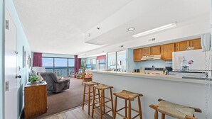 A modern kitchen with wooden bar stools, a dining area with a view, and a small kitchenette. - Oceans 816 - Great Views - 1 Bedroom Ocean Front Condo (North Myrtle Beach)