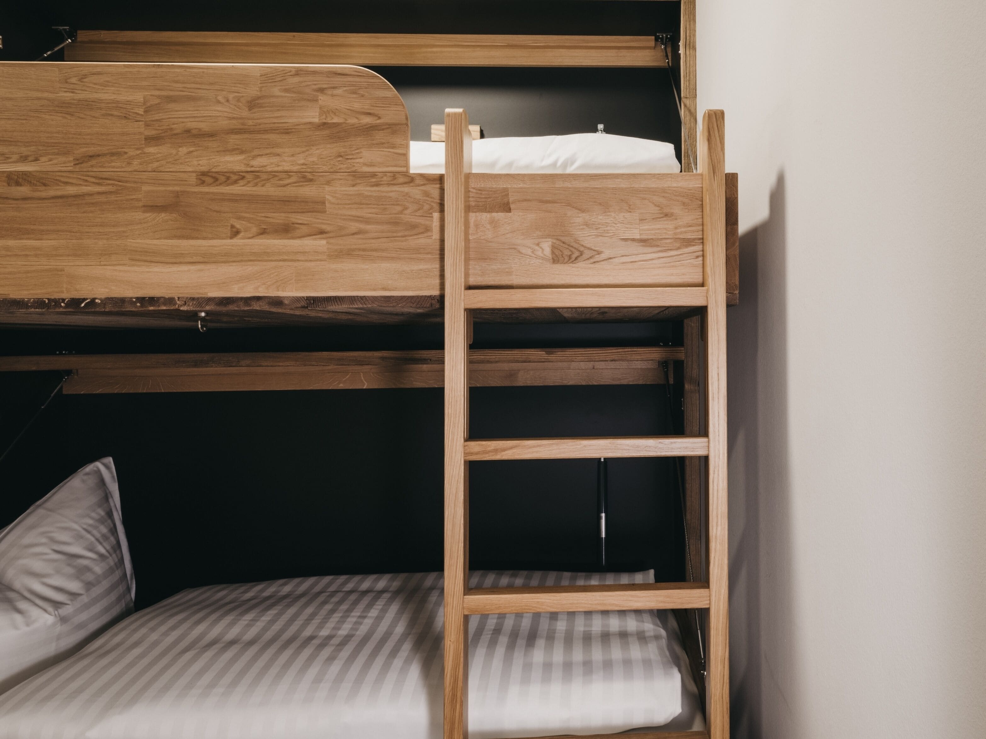 Una cama litera con escalera de madera, una cama individual abajo y una pared negra.