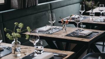 Een restaurant met houten tafels, glazen servies en een bloemenvaas.