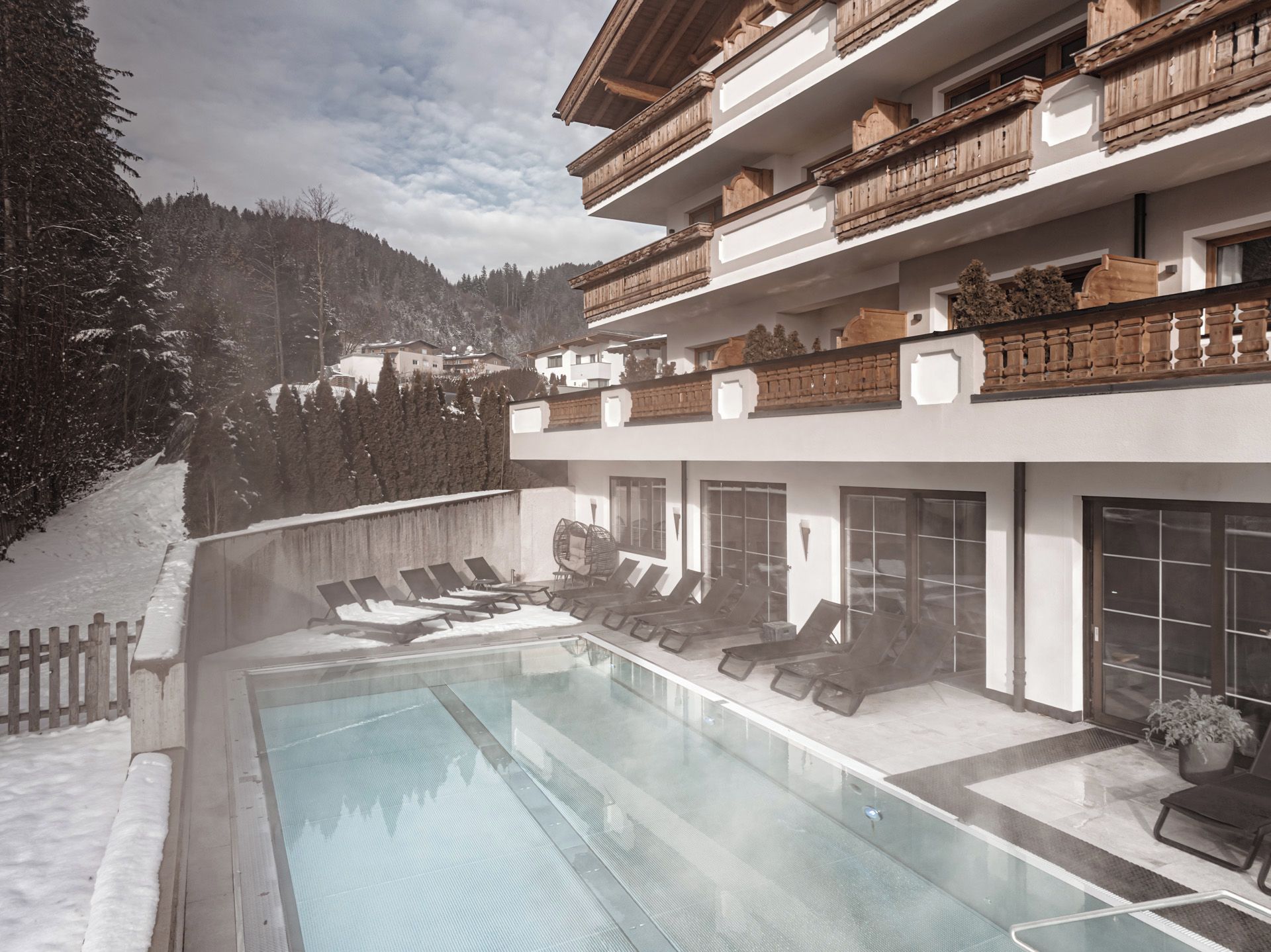 Ein modernes Hotel mit Pool, Liegestühlen und Blick auf schneebedeckte Berge.