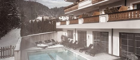 A modern hotel with a pool, lounge chairs, and a view of snow-covered mountains.