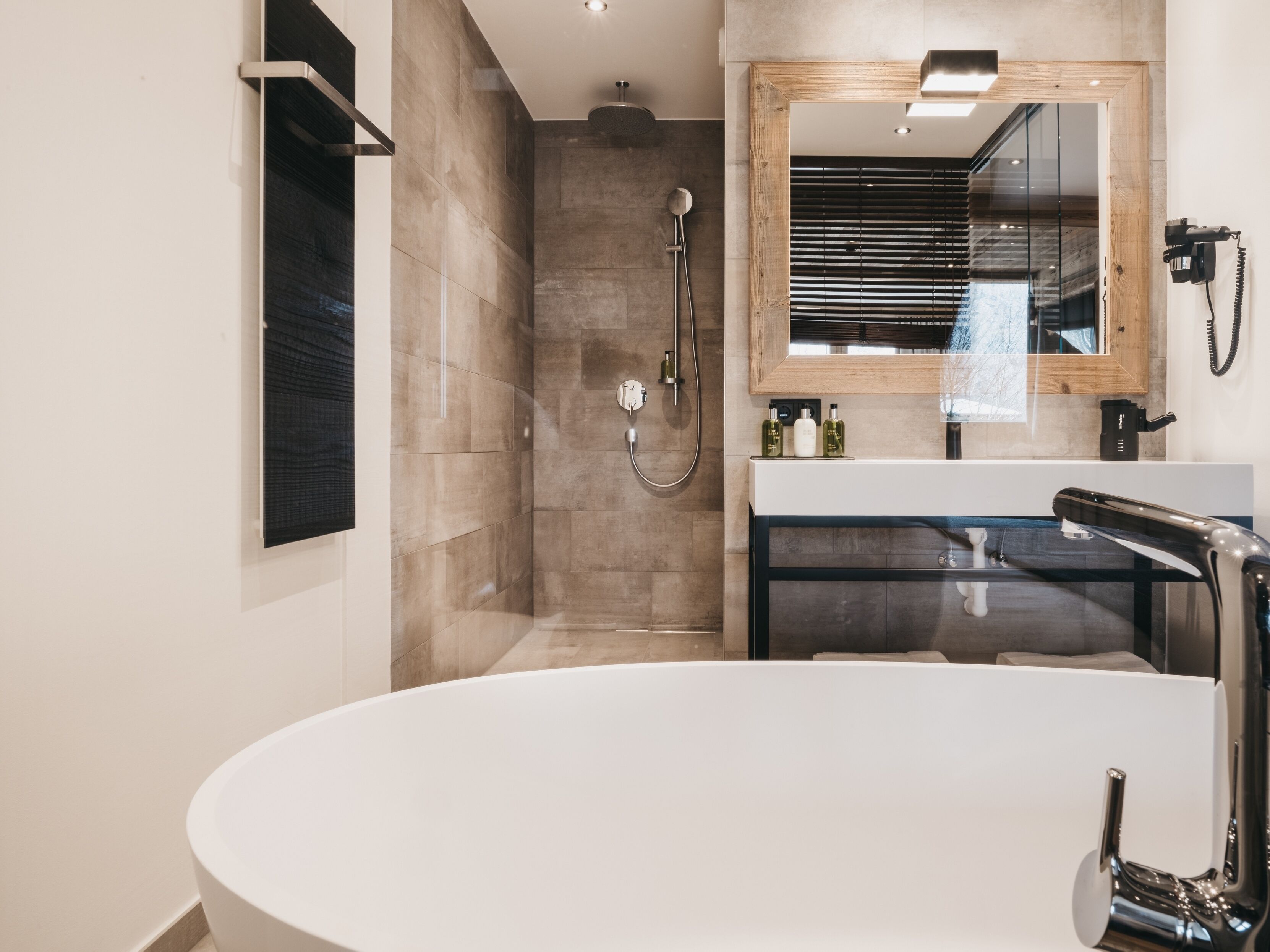 Een moderne badkamer met een vrijstaand bad, een douchecabine met glazen wanden en een spiegel met houten lijst.
