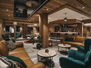 A spacious lounge area with leather sofas, a bar, and a large clock on the wall. - VAYA Zillertal (Aschau Im Zillertal)