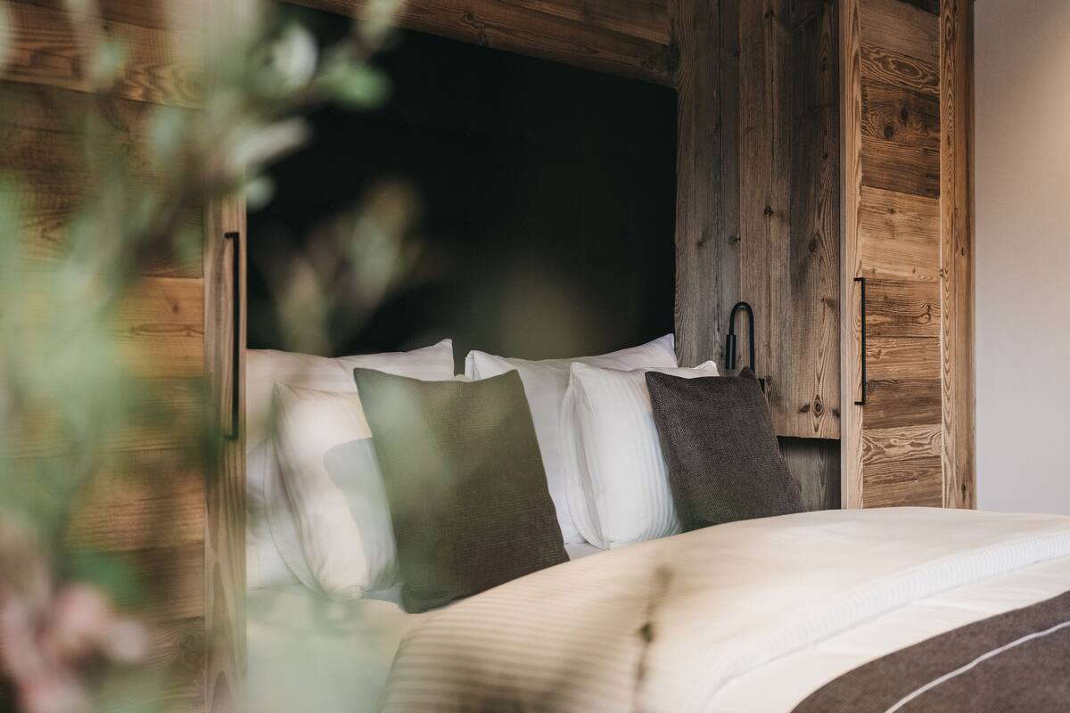 Een bed met wit- en bruin beddengoed, een houten hoofdbord en een klein nachtkastje met een lamp.