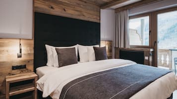 A bedroom with a wooden ceiling, a large bed with white and dark pillows, a nightstand, and a window with a view of a snowy landscape.