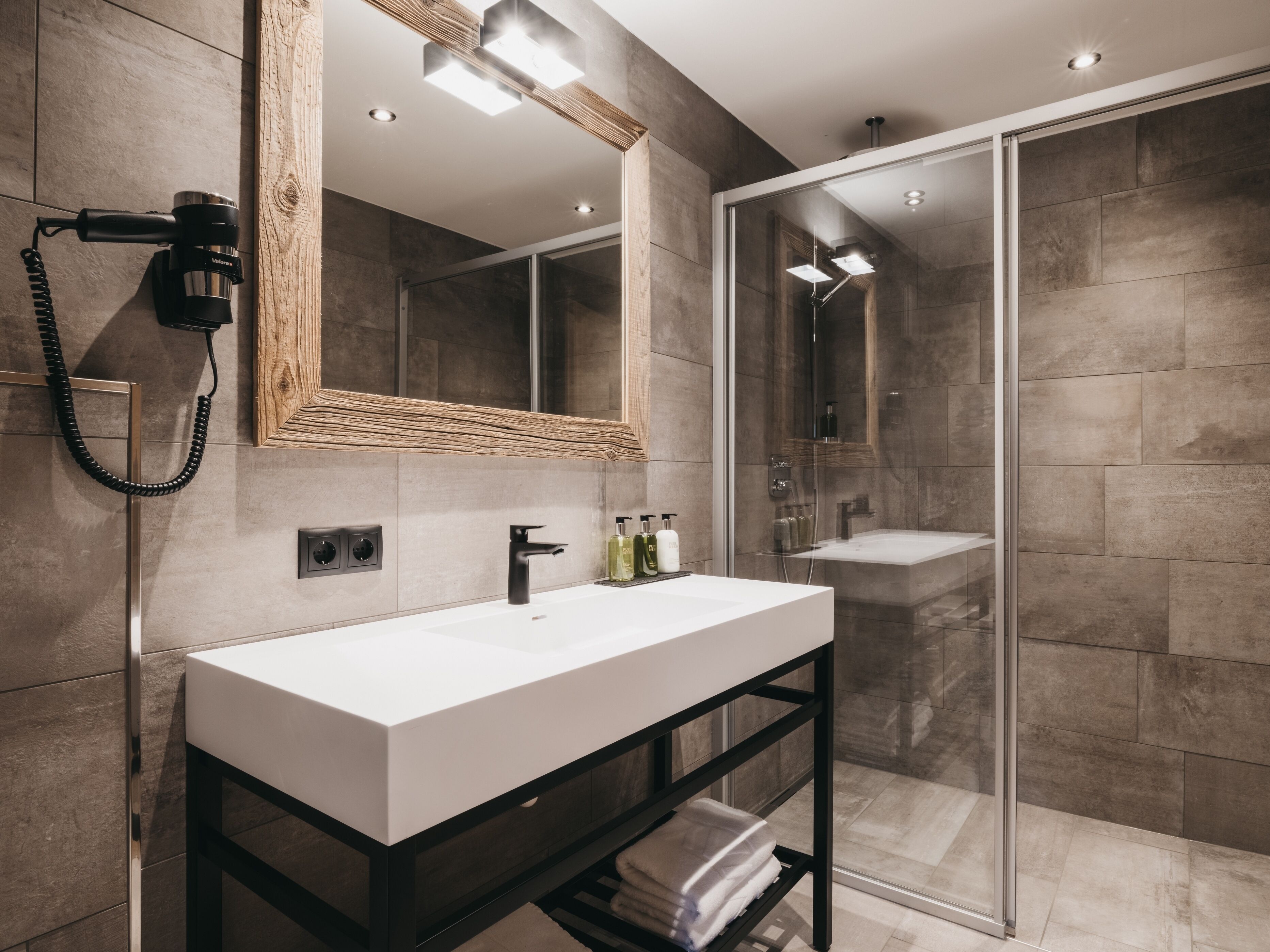 A modern bathroom with a large mirror, a white sink, a black vanity, and a glass-enclosed shower.