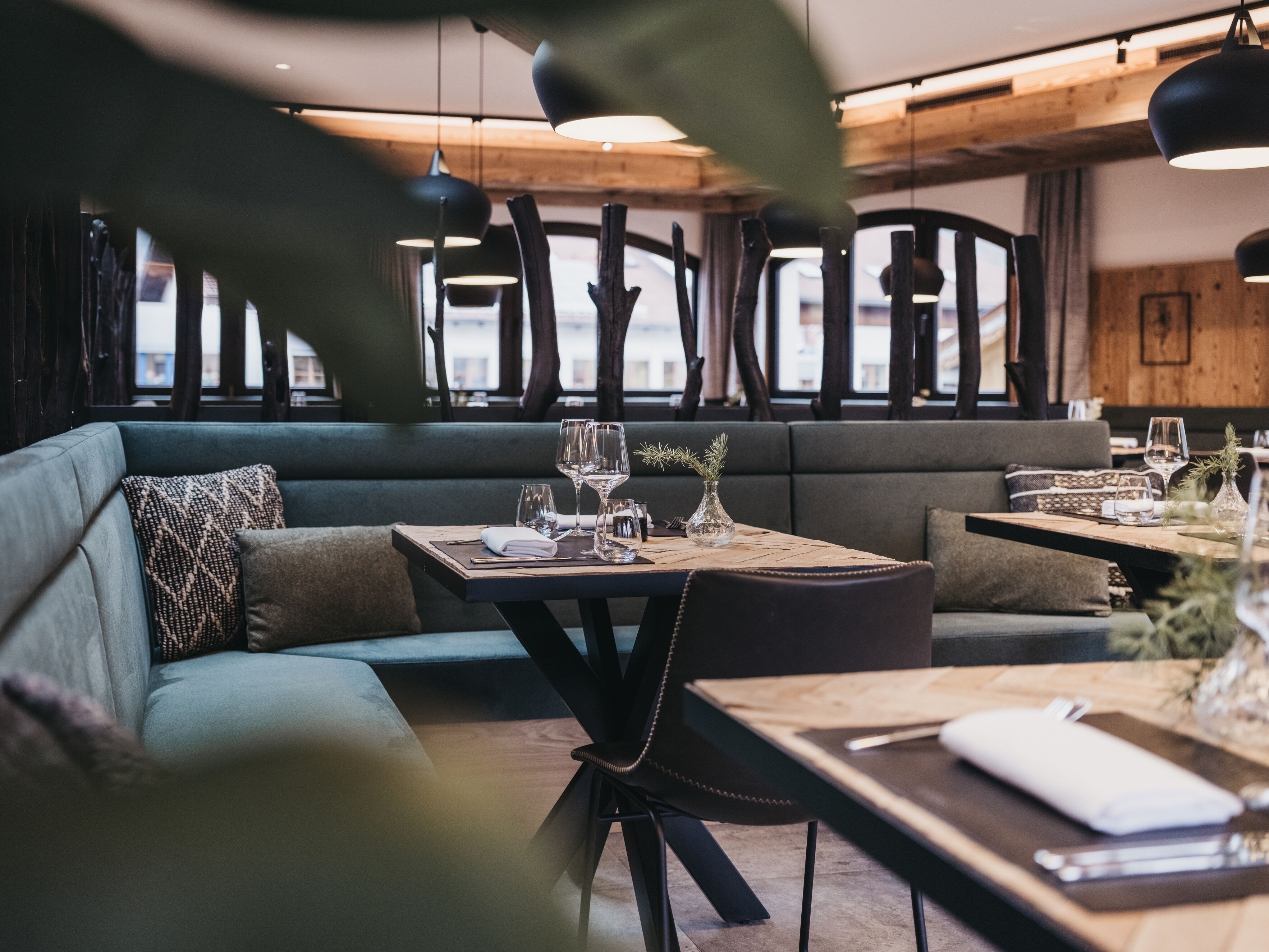 L’intérieur d’un restaurant, avec un plafond en bois, un canapé recouvert d’un tissu vert et une table dressée pour le repas.