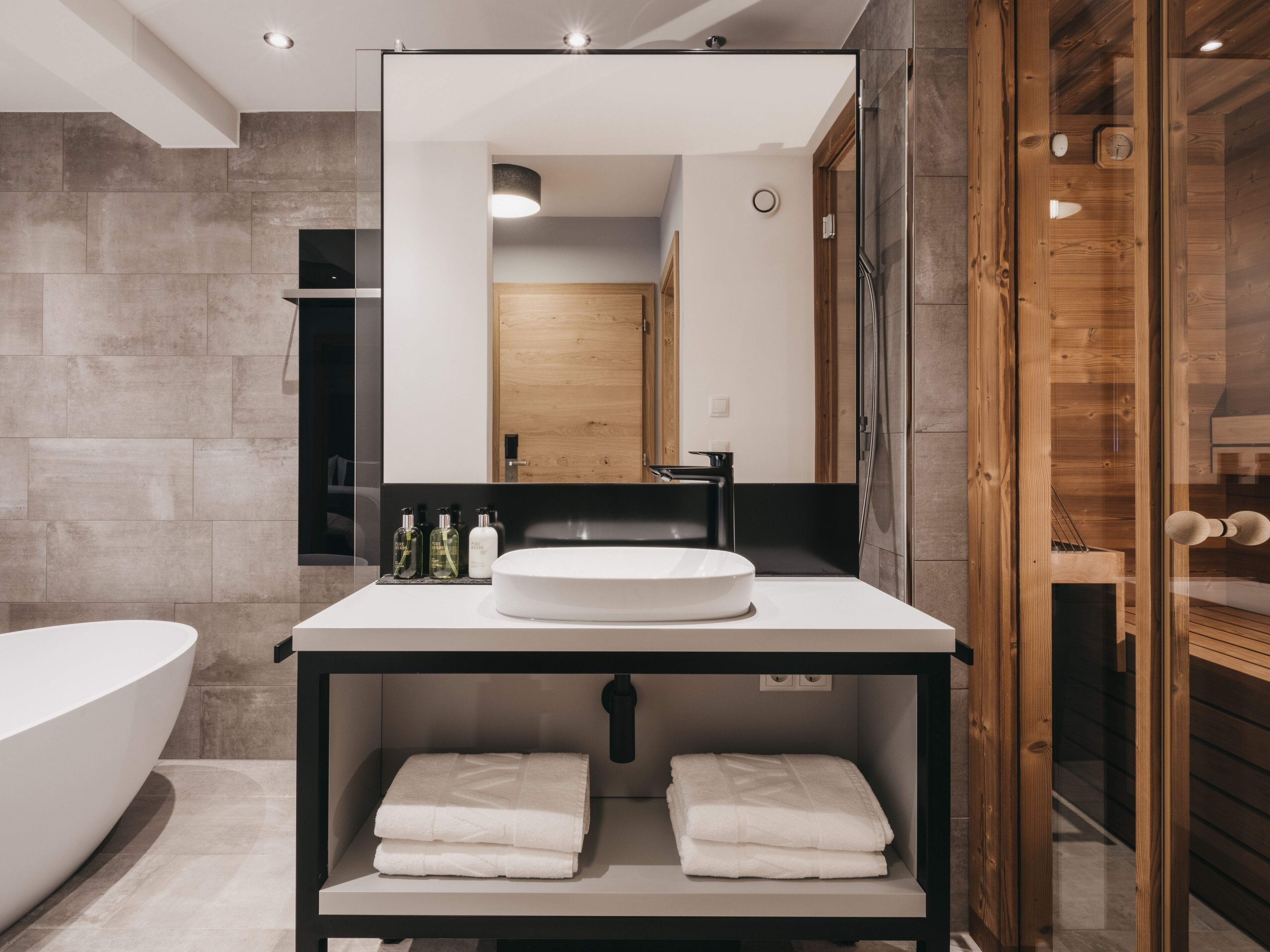 Ein modernes Badezimmer mit einem großen Spiegel, einem weißen Waschbecken und einer Dusche mit Holzelementen.