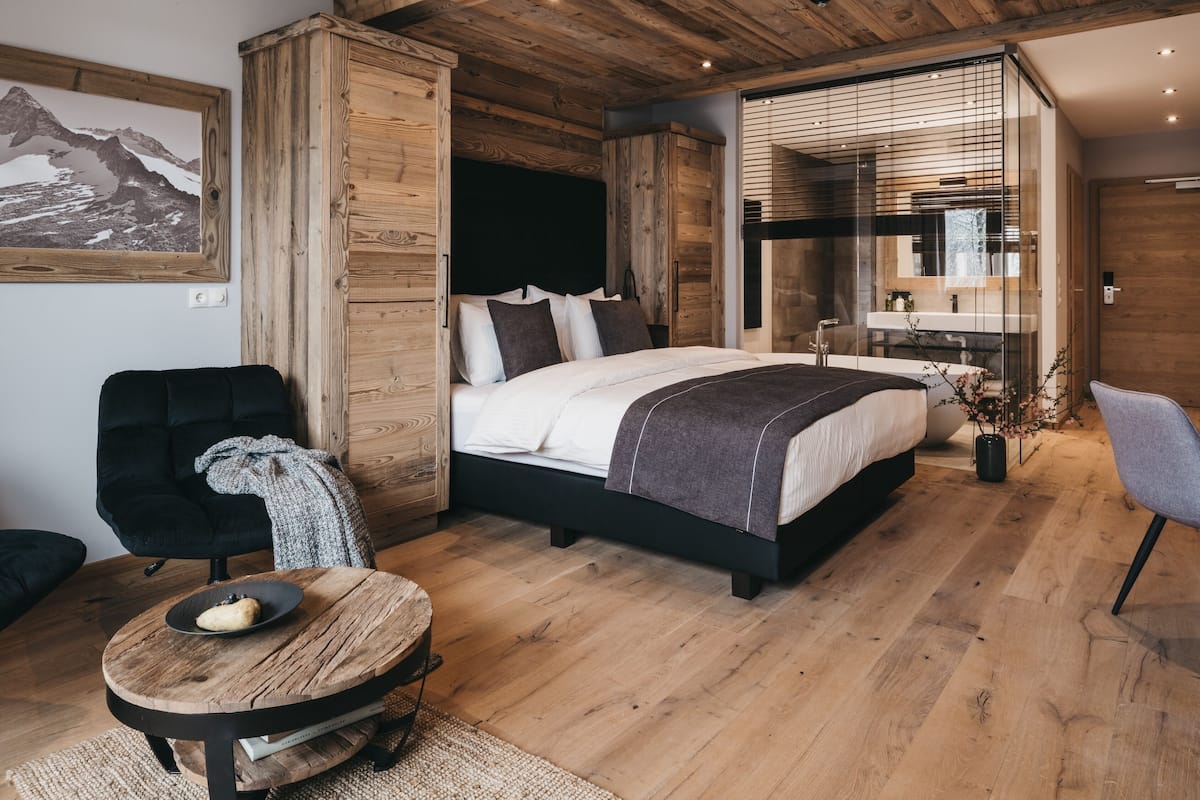 Een moderne slaapkamer met een houten plafond, een groot bed, een nachtkastje met een lamp, een stoel en een klein rond tafeltje met een kom.