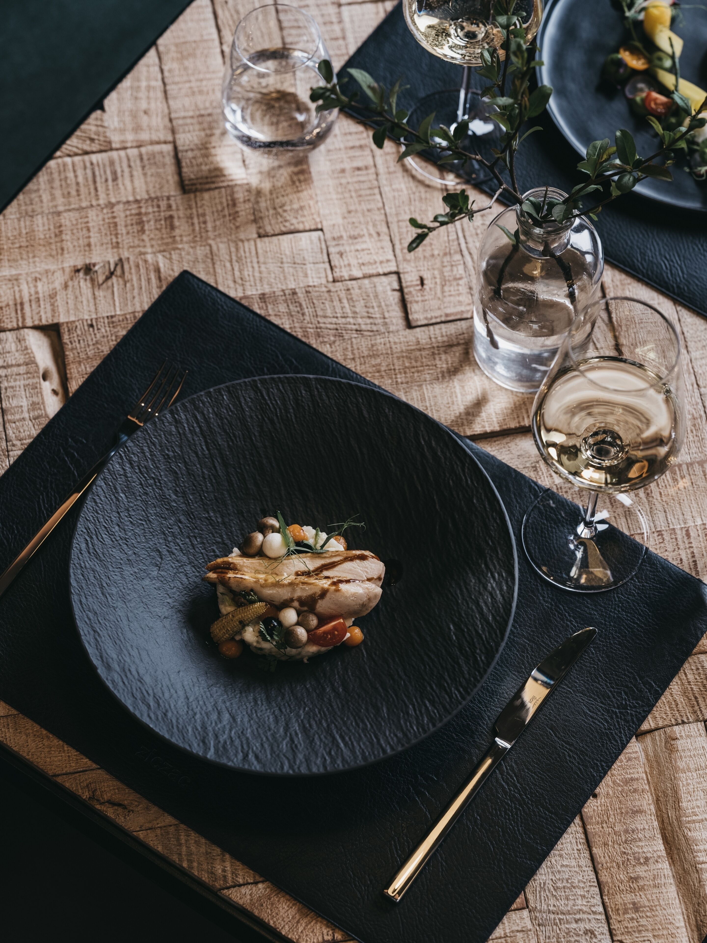 A dining table with a black plate, a glass of water, and a glass of wine.