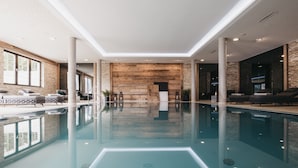 Un área de piscina interior moderna con una piscina cristalina, sillas de descanso y una pared de madera.
