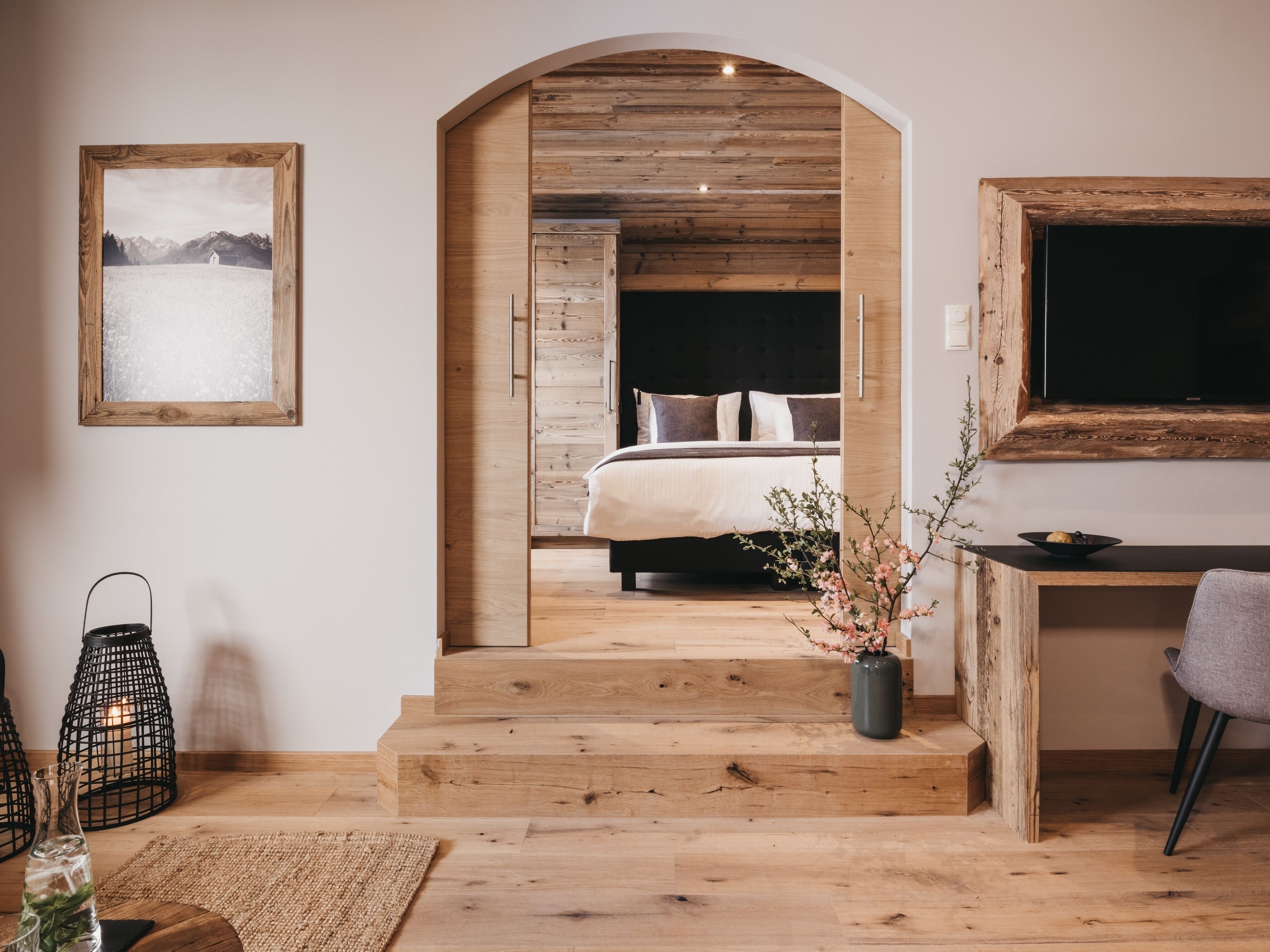 A modern bedroom with a wooden staircase leading to a bed, a desk, and a television.