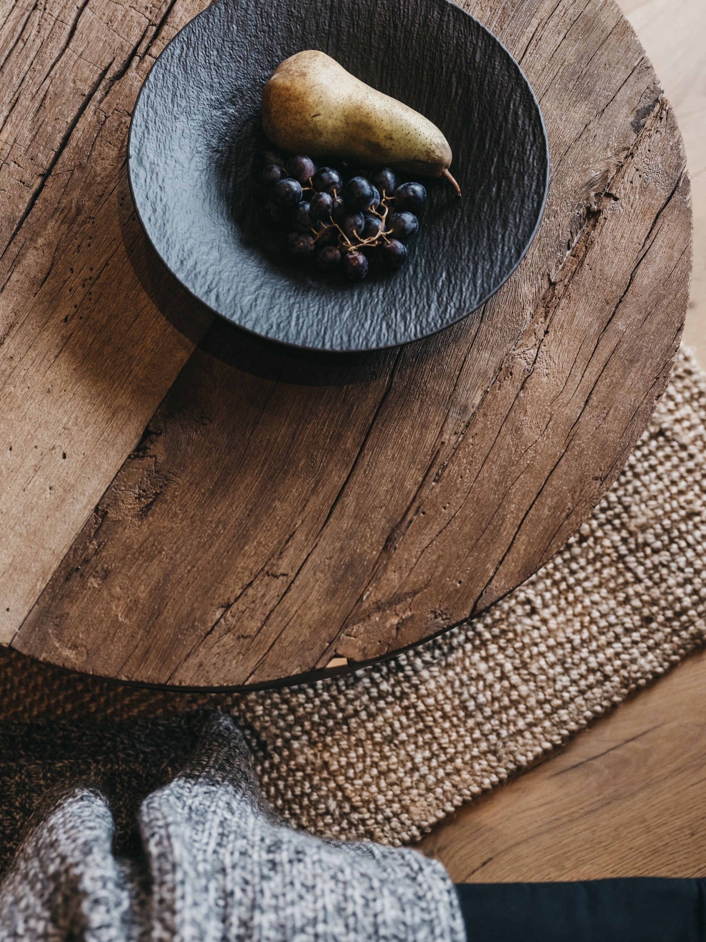 A wooden table with a black plate containing a pear and grapes.