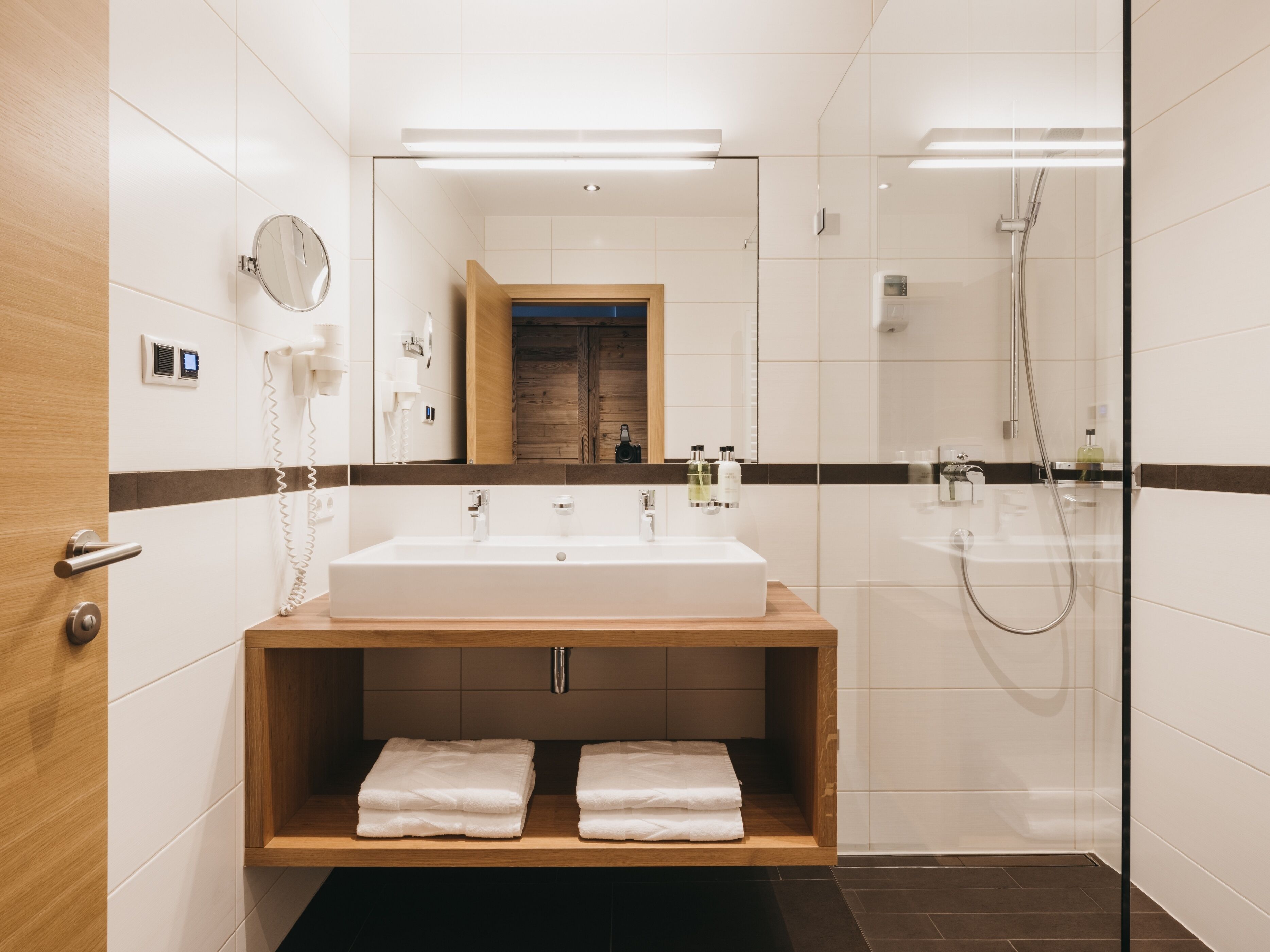 Ein modernes Badezimmer mit einem großen weißen Waschbecken, einem Holzlager und einer Glasdusche sowie einem Spiegel.